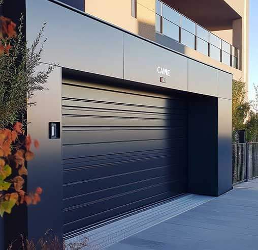 A modern garage with sleek black horizontal panels set in an upscale, minimalist building. Sunlight casts subtle shadows; a nearby plant adds warmth.